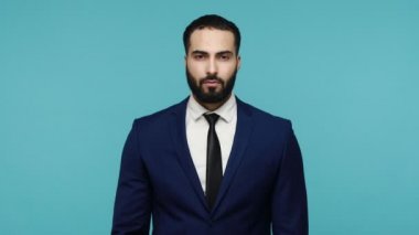 Hey sen, bana gel! Resmi siyah takım elbiseli, sakallı yakışıklı esmer adam kameraya ciddi bir yüz ifadesiyle bakıyor, davetkar hareketler yapıyor. Mavi arka planda kapalı stüdyo çekimi.