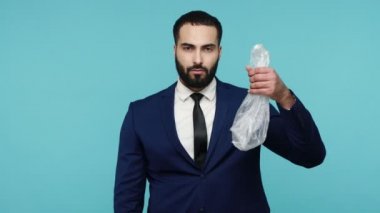 Sakallı yakışıklı işadamı geri dönüşümlü eko konteynırı seçiyor, plastik ve kağıt paketler arasında seçim yapıyor, çevre kirliliği kavramı. Mavi arka planda kapalı stüdyo çekimi.