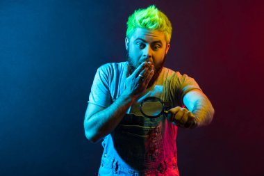 Yeşil saçlı çekici hippi adam elinde tulum tutan, suç mahallini inceleyen, şaşırtıcı şeyler gören, ağzı avuç içiyle kaplı. Renkli neon ışık, kapalı stüdyo çekimi..