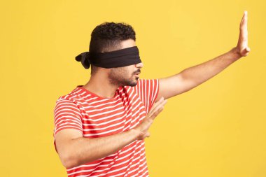 Profil portresi sakallı, görme sorunu olan siyah bandajlı, elleri uzanan, dokunarak yön bulmayı öğrenen, duyuları gelişen bir adam. Sarı arka planda kapalı stüdyo çekimleri