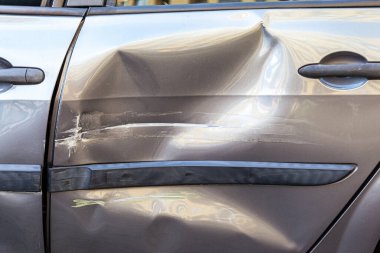 Bir yolda kaza yaptıktan sonra arabanın hasarlı arka kapısının kapanması, araba gövdesinde ezikler ve çizikler, kazadan sonra otomobilin yan tarafının tahrip olması..