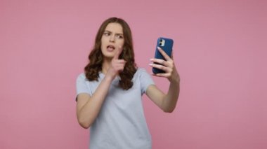 Güzel arkadaş canlısı blogcu kız cep telefonuyla çevrimiçi yayın yoluyla denizaltılarla iletişim kuruyor, tıklamak ve abone olmak istiyor. Pembe arka planda kapalı stüdyo çekimleri.