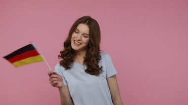 Neşeli vatansever genç kız Alman bayrağı sallıyor ve gülümsüyor, mutluluğunu ifade ediyor, Bağımsızlık Günü ulusal bayramını kutluyor. Pembe arka planda kapalı stüdyo çekimleri.