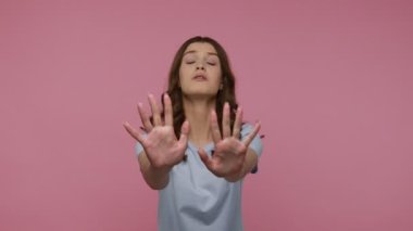 Genç, korkmuş, tedirgin, koyu saçlı genç kız elleriyle blokluyor, kabus yüzünden hayal kırıklığına uğruyor, dur hareketi gösteriyor. Pembe arka planda kapalı stüdyo çekimleri.