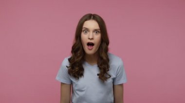 Kahverengi dalgalı saçlı, tişörtlü mutlu ve neşeli genç kız piyango zaferini ve başarısını kutluyor. Pembe arka planda kapalı stüdyo çekimleri.
