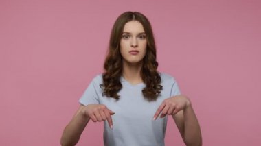 Aşırı mutluluk ve şaşkınlık ifadesiyle parmağını aşağı gösteren dalgalı saçlı tutkulu kadın, bak ve aşağıdaki bilgiyi takip et. Pembe arka planda kapalı stüdyo çekimleri.