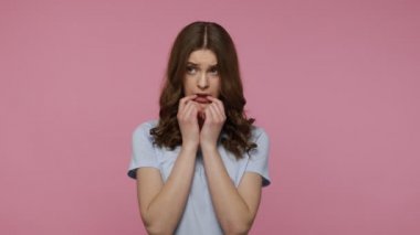 Depresyon, üzüntü, olumsuz duygular. Üzgün dalgalı saçlı, mavi tişörtlü sinirli sinirli sinirli görünen tırnak yiyen bir kız. Pembe arka planda kapalı stüdyo çekimleri.