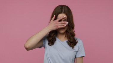 Sıradan tişörtler giyen, meraklı bir ifadeyle parmaklarının arasından gizlice bakan, izlemekten çekinen, gizli bilgileri gözetleyen genç bir kadın. Pembe arka planda kapalı stüdyo çekimleri.