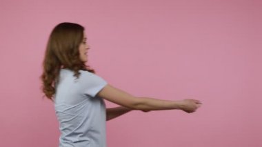Maksatlı dalgalı saçlı genç kızın görünmeyen ipi çekmesi kadın haklarıyla mücadele kavramı, cinsiyet eşitliği. Pembe arka planda kapalı stüdyo çekimleri.