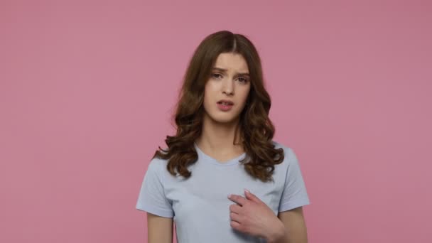 青いTシャツを着た愛らしい失望した10代の少女は 危機のために不幸な皮肉と負け犬のサインを示す額の近くに指を握っています 屋内スタジオはピンクの背景に隔離されたショット — ストック動画