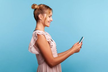 İki tüylü popolu arkadaş canlısı bayanın profili, cep telefonundan veya yayın akışından video görüşmesi yapıyor, internet iletişimi için cihaz kullanıyor. Mavi arka planda kapalı stüdyo çekimi.