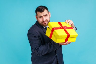 Hediye kutusu açık sakallı, üzgün, meraklı bir adamın portresi. Hediyesini almak için hediyesini açıyor. Hayal kırıklığına uğramış ve hayal kırıklığına uğramış. Mavi arka planda kapalı stüdyo çekimi.