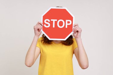 Yasaktır! Sarı günlük tişörtlü, üzerinde kırmızı trafik işareti olan, kırmızı tişörtlü, kimliği belirsiz bir kızın portresi. Gri arka planda izole edilmiş kapalı stüdyo görüntüleri.