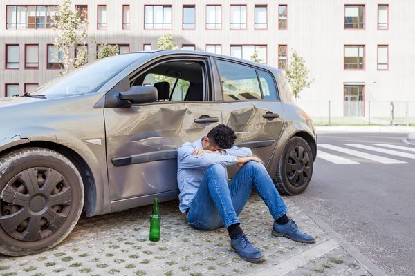 Mężczyzna Dżinsach Niebieskiej Koszuli Siedzący Pobliżu Rozbitego Samochodu Butelką Alkoholu — Zdjęcie stockowe