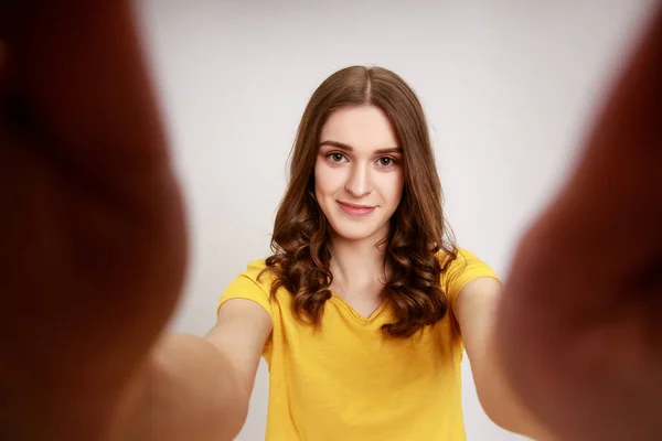 黄色のカジュアルなTシャツに身を包んだ可愛い10代の少女が ポジティブな気持ちでカメラを見ている姿を描いていますPov 灰色の背景に隔離された屋内スタジオショット — ストック写真