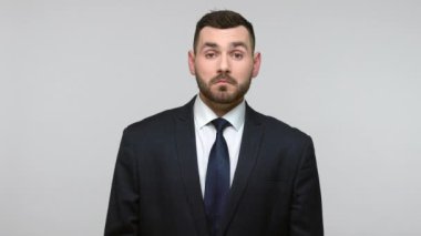 Siyah resmi takım elbiseli, gülümseyen sakallı bir iş adamının portresi kameraya bakıyor ve başparmağını kaldırıyor, servis öneriyor. Gri arka planda izole edilmiş kapalı stüdyo görüntüleri.