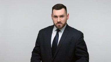 Siyah takım elbiseli, yumruklarını sıkmış, kameraya yumruk atan, saldırmakla tehdit eden kızgın, genç, sakallı bir iş adamı. Gri arka planda izole edilmiş kapalı stüdyo görüntüleri.