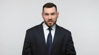 Siyah resmi takım elbiseli agresif sakallı iş adamı kameraya bakıyor ve seni seçiyor. Öfke ve hayal kırıklığını ifade ediyor. Gri arka planda izole edilmiş kapalı stüdyo görüntüleri.