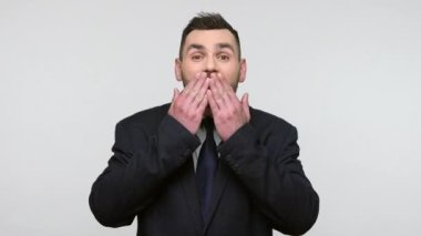 Siyah resmi takım elbiseli romantik sakallı iş adamı hava öpücüğü gönderiyor, dudaklarını büzüyor, kadın çalışanlarıyla flört ediyor, sevgisini ifade ediyor. Gri arka planda izole edilmiş kapalı stüdyo görüntüleri.