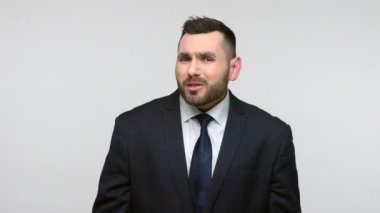 Siyah resmi takım elbiseli meraklı sakallı iş adamının portresi seslere odaklanıyor, sohbet duymaya çalışıyor. Gri arka planda izole edilmiş kapalı stüdyo görüntüleri.