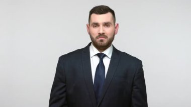 Siyah resmi takım elbiseli hoşnutsuz sakallı iş adamı. Başparmaklarını göstermiyor. Hoşnutsuzluğun sembolü, geri bildirim veriyor. Gri arka planda izole edilmiş kapalı stüdyo görüntüleri.