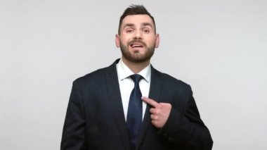 Siyah resmi takım elbiseli, gururlu, sakallı bir iş adamı. Kendini beğenmiş, kendini beğenmiş, ünlü hissediyor. Gri arka planda izole edilmiş kapalı stüdyo görüntüleri.