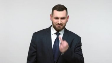 Siyah resmi takım elbiseli sakallı iş adamı orta parmağını gösteriyor ve kameraya olumsuz ve saygısız bir tavırla bakmaktan vazgeçmek istiyor. Gri arka planda izole edilmiş kapalı stüdyo görüntüleri.