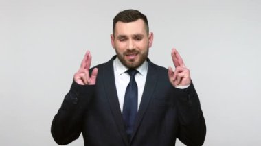 Siyah resmi takım elbiseli genç ve sakallı bir iş adamı şans dilemek için şans diliyor başarıyı kutluyor ve mutlu bir şekilde bağırıyor. Gri arka planda izole edilmiş kapalı stüdyo görüntüleri.