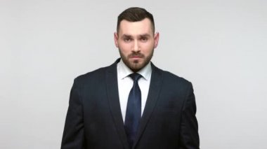 Burada ve şimdi! Siyah resmi takım elbiseli ciddi sakallı iş adamı küstahça bakıyor ve derhal itaat talep ediyor. Gri arka planda izole edilmiş kapalı stüdyo görüntüleri.