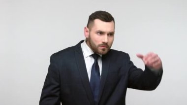 Siyah resmi takım elbiseli sakallı işadamı avucunu kapalı tutuyor ve dikkatle uzaklardan bakıyor. Uzun mesafeden beklentileri var. Gri arka planda izole edilmiş kapalı stüdyo görüntüleri.