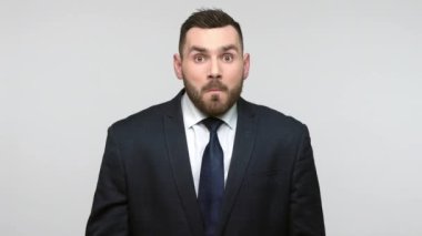 Siyah resmi takım elbiseli, hayret verici genç, sakallı iş adamı inanılmaz haberler duyuyor, sır saklıyor, fermuar hareketleri yapıyor. Gri arka planda izole edilmiş kapalı alan çekimleri..