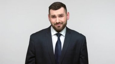 Siyah resmi takım elbiseli, hoşnutsuz sakallı iş adamının portresi. Minimum boyda, kuşkulu ve hayal kırıklığına uğramış görünüyor. Gri arka planda izole edilmiş kapalı stüdyo görüntüleri.