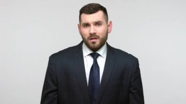 Siyah resmi takım elbiseli sakallı işadamı X işaretinde silah çekmeyi reddediyor, jesti durduruyor, erişimi yasaklıyor, iletişimi kesiyor. Gri arka planda izole edilmiş kapalı stüdyo görüntüleri.