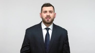 Siyah resmi takım elbiseli sakallı iş adamı facepalm hareketi yapıyor. Üzüntü ifadesiyle başını okşuyor. Belaya karşı çaresiz. Gri arka planda izole edilmiş kapalı stüdyo görüntüleri.