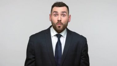 Siyah resmi takım elbiseli komik, pozitif sakallı iş adamı büyük gözlü, suratsız, komik suratlı balık suratı yapıyor. Gri arka planda izole edilmiş kapalı stüdyo görüntüleri.