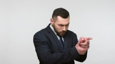 Tehlikeli, kendine güvenen, takım elbiseli sakallı iş adamı. Parmak tabancalarıyla tehdit ediyor, kameraya ateş ediyor, el kol hareketi yapıyor ve öldürüyor. Gri arka planda izole edilmiş kapalı stüdyo görüntüleri.