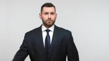 Resmi takım elbiseli, sakallı, genç, yetişkin bir iş adamı. Başının yanında el ele tutuşmuş. Sorumlu bir ifadeyle selam veriyor ve dinliyordu. Gri arka planda izole edilmiş kapalı stüdyo görüntüleri.