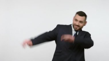 Siyah resmi takım elbiseli sakallı işadamı, başarıyı dans figürleriyle kutluyor, ünlü internet zafer mim 'i, dokunaklı trendler sergiliyor. Gri arka planda izole edilmiş kapalı stüdyo görüntüleri.