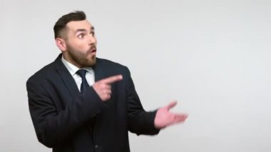 Siyah resmi takım elbiseli sakallı iş adamının palmiye üzerinde şok edici bir yüz ifadesi olan kopya alanını sunmasına şaşırdım. Gri arka planda izole edilmiş kapalı stüdyo görüntüleri.