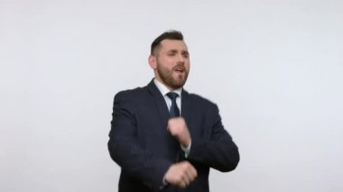 Son derece mutlu sakallı iş adamı resmi siyah takım elbiseli dans ediyor ve ritme ayak uyduruyor, olumlu duygular ifade ediyor, kutluyor. Gri arka planda izole edilmiş kapalı stüdyo görüntüleri.