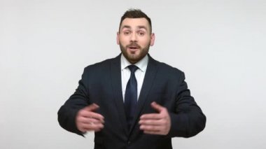 Siyah resmi takım elbiseli, dost canlısı, nazik sakallı iş adamı kucaklaşmak için ellerini sonuna kadar açık tutuyor, sıcak sarılıyor ve dostça karşılıyor. Gri arka planda izole edilmiş kapalı stüdyo görüntüleri.