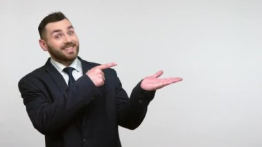 Resmi takım elbiseli, güler yüzlü, sakallı iş adamı bir yana, fotokopi çekilen yeri göstererek mutlu bir ifadeyle kameraya bakıyor. Gri arka planda izole edilmiş kapalı stüdyo görüntüleri.