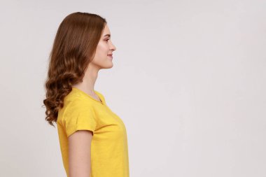 Sarı günlük tişörtlü, gülümseyen, mutlu ve memnun görünen, reklam için boş fotokopi odası olan başarılı bir kadının yan görüntüsü. Gri arka planda izole edilmiş kapalı stüdyo görüntüleri.