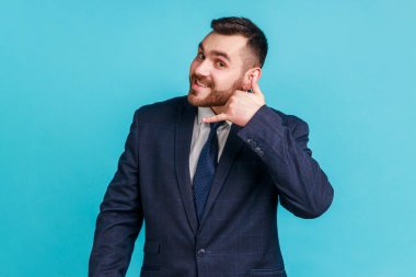 Ara beni! Sakallı, yakışıklı, neşeli bir adamın portresi. Kulağının dibinde telefonla el hareketi yapıyor, telefonda iletişimi taklit ediyor. Mavi arka planda kapalı stüdyo çekimi.