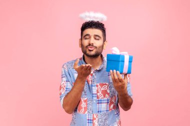 Mavi tişörtlü, sakallı, mavi gömlekli bir adam hediye kutusunu tutuyor ve kameraya hava öpücüğü gönderiyor. Aşkı ve romantizmi ifade ediyor..