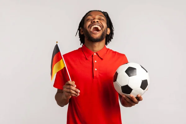 尖叫的男子身穿红色休闲装T恤 足球迷由衷地欢欣鼓舞 支持最喜爱的球队持球和德国国旗 观看足球 在灰色背景下被隔离的室内拍摄 — 图库照片