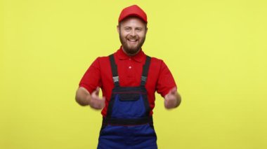 Mutlu pozitif işçi, başparmağını kaldırıyor ve kameraya bakıyor. Bakım hizmeti öneriyor. Mavi üniforma, kırmızı tişört ve güneşlik takıyor. Sarı arka planda izole edilmiş kapalı stüdyo çekimi.