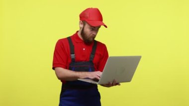 Kafası karışmış bir işçi defteri elinde tutuyor ve olumsuz duygularını dile getiriyor, neden diye bağırıyor, mavi üniforma, kırmızı tişört ve güneşlik şapkası giyiyor. Sarı arka planda izole edilmiş kapalı stüdyo çekimi.