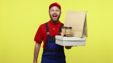 Teslimatçı siparişler için indirimler sunar, pakette yiyecek ve kahve bulundurur, satış kartı gösterir, mavi üniforma, kırmızı tişört ve şapka giyer. Sarı arka planda izole edilmiş kapalı stüdyo çekimi