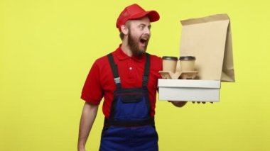 Afallamış teslimatçı elinde yiyecek ve kahveyle gidip kumbarayı gezdirecek, para biriktirecek mavi üniforma, tişört ve şapka takacak. Sarı arka planda izole edilmiş kapalı stüdyo çekimi.